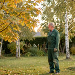 Quels arbres choisir pour ne pas les tailler en septembre au jardin ? Un homme jardinier observe les branches d’un grand érable et d’un bouleau aux feuilles légèrement jaunissantes dans un jardin familial en septembre.